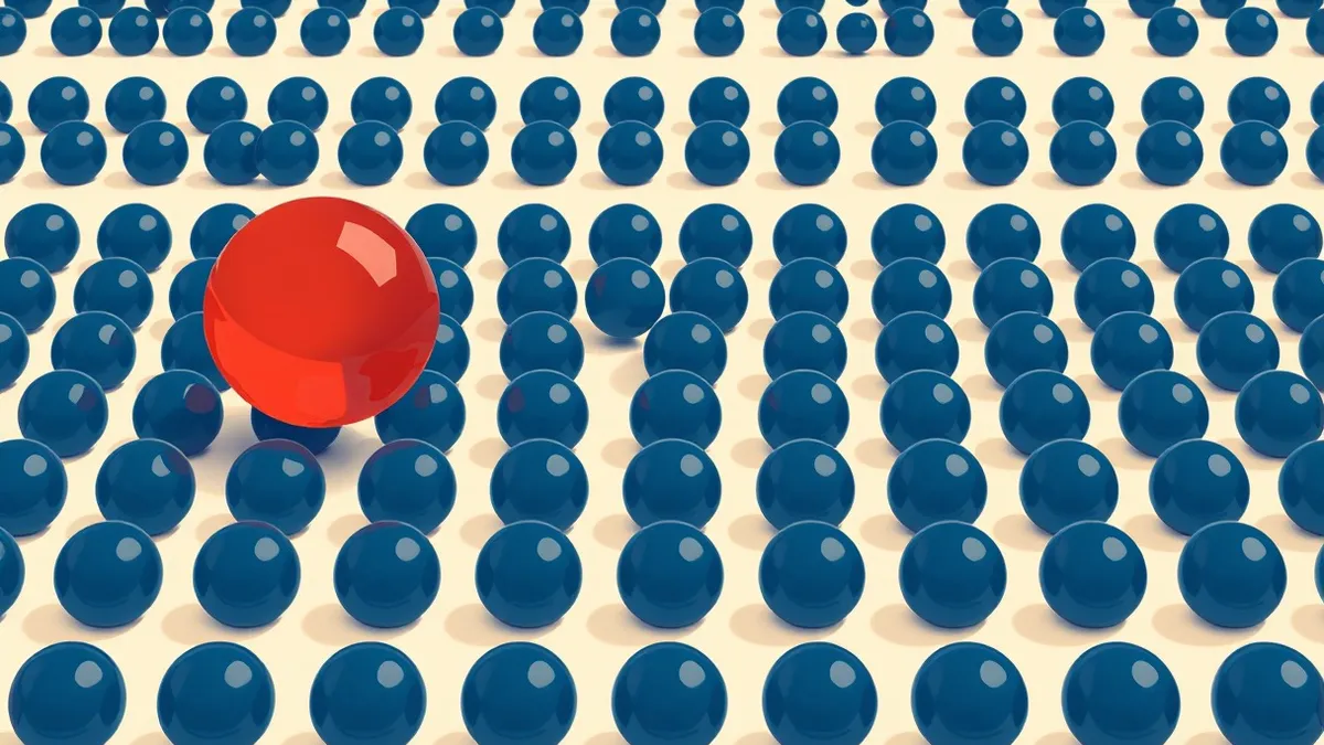 Illustration: A single distorted red marble rolls among thousands of identical blue glass spheres on a white table.